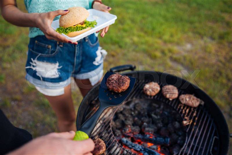 Top view of young people cooking hamburger and cooking meet on barbeque grill outdoors, stock photo