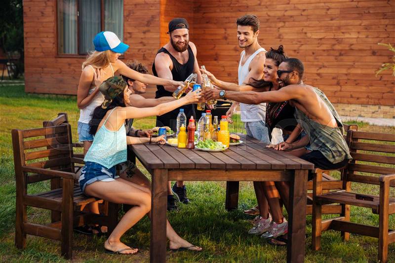 Group of happy young people celebrating and drinking beer and soda at the table outdoors, stock photo