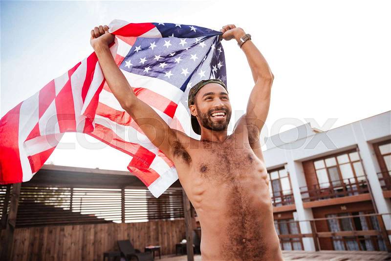Smiling afro american shirtless man holding american flag outdoors, stock photo