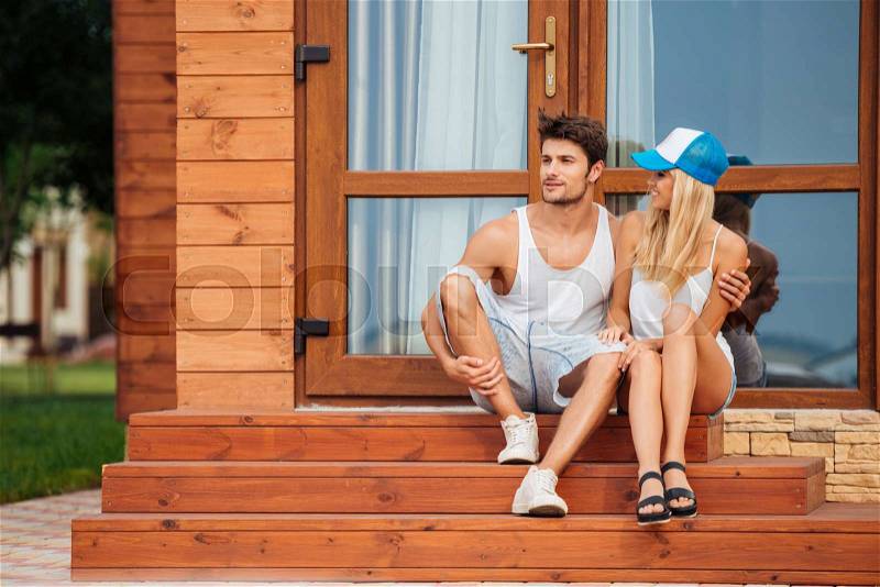 Happy beautiful young couple sitting on porch of wooden house in summer, stock photo