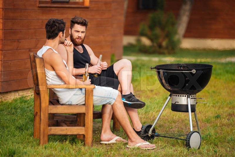 Two young men talking while preparing barbecue grill in park zone, stock photo