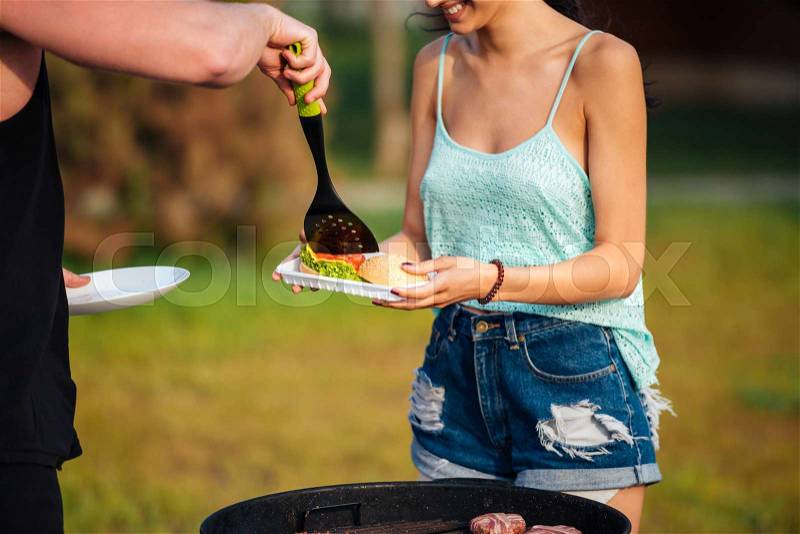 Closeup of happy young couple frying meet and making hamburgers outdoors, stock photo