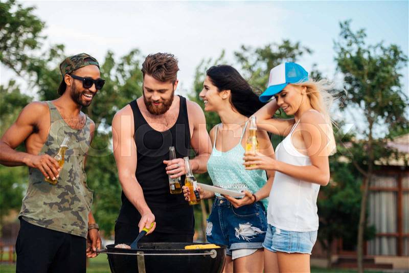 Group of happy young people standing and frying meet on barbeque grill outdoors, stock photo