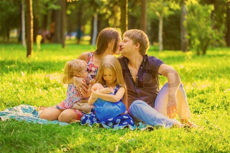 Happy family together at the picnic. Mother breastfeeding baby son, little daughter is breastfeeding a doll, stock photo