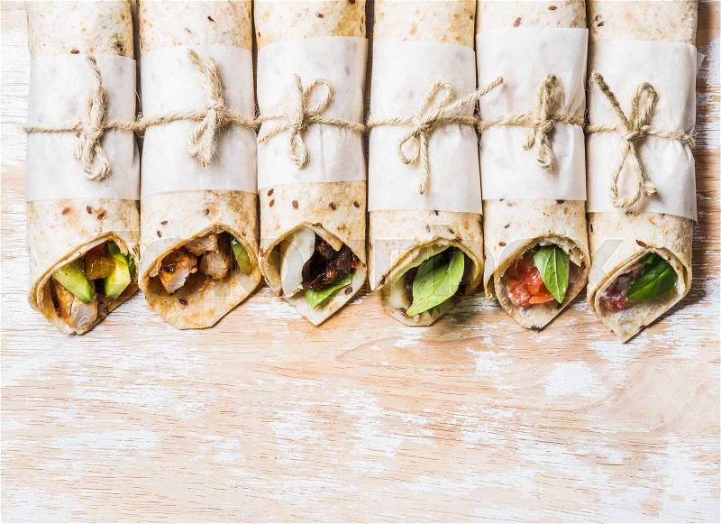 Tortilla wraps with various fillings on shabby painted board over white wooden background, top view, copy space, horizontal composition. Healthy snack or take-away lunch bites, stock photo