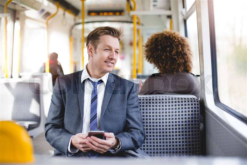 Formal businessman sitting on the train. He is holding a smartphone and looking out the window. , stock photo