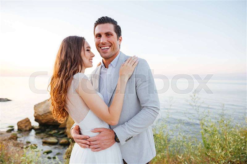 Romantic married couple standing and laughing on the beach at sunset, stock photo