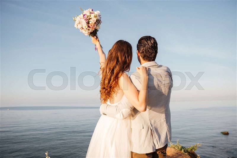 Back view of a romantic happy married couple standing at the beach, stock photo