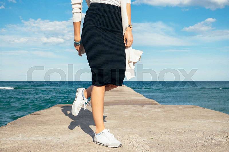Details of women\'s clothing: Female legs in a skirt and sneakers on the background of the sea, stock photo