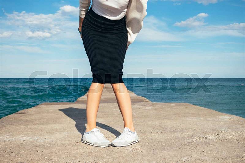 Women\'s legs in a skirt on a background of the sea in summer, stock photo