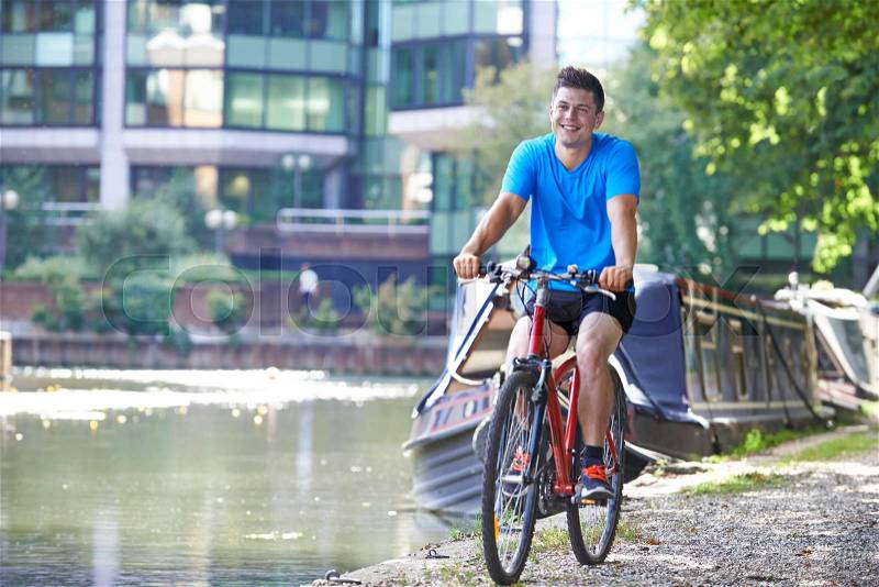 Young Man Cycling Next To River In Urban Setting, stock photo