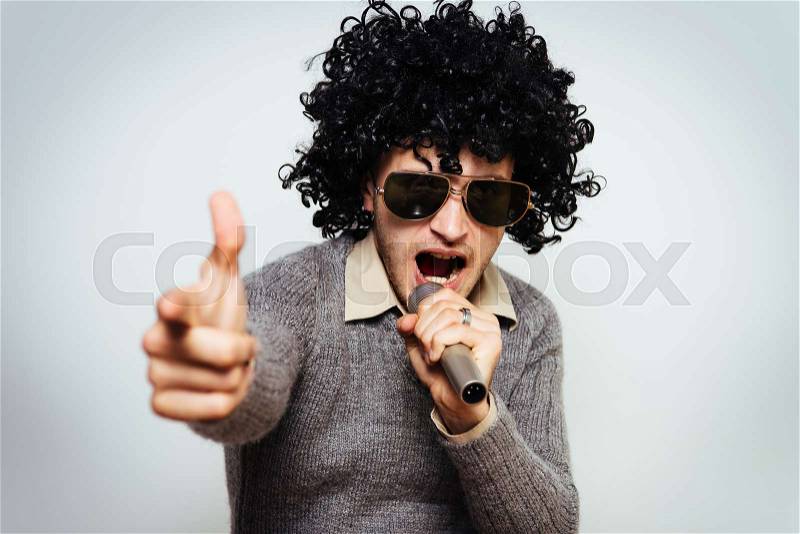 A man in a wig, and sunglasses singing into a microphone, stock photo