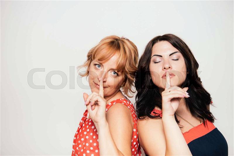 Portrait of two attractive women with finger on lips, stock photo