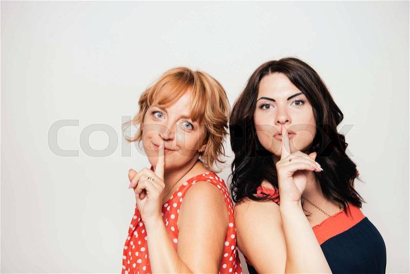 Portrait of two attractive women with finger on lips, stock photo