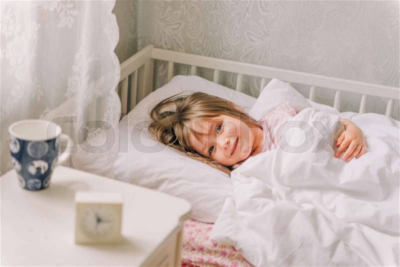Little girl lying in bed. Little girl dressed in pajamas, lying in bed and smiling, stock photo