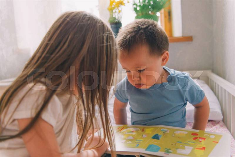 Little girl and boy read the book. sister and brother watching book. small boy sits in bed and sees a book. little girl is considering a book with him. children read and watch pictures in the book, stock photo