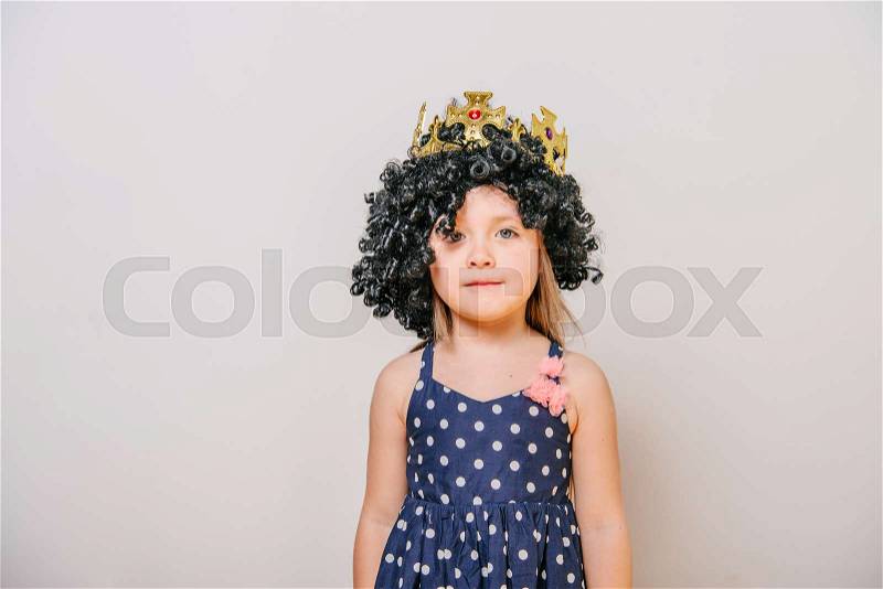 Girl with crown. little girl with a crown. funny little girl in a wig and crown. Girl looks funny. Curly little girl in a black wig. little girl in a dress and crown, stock photo