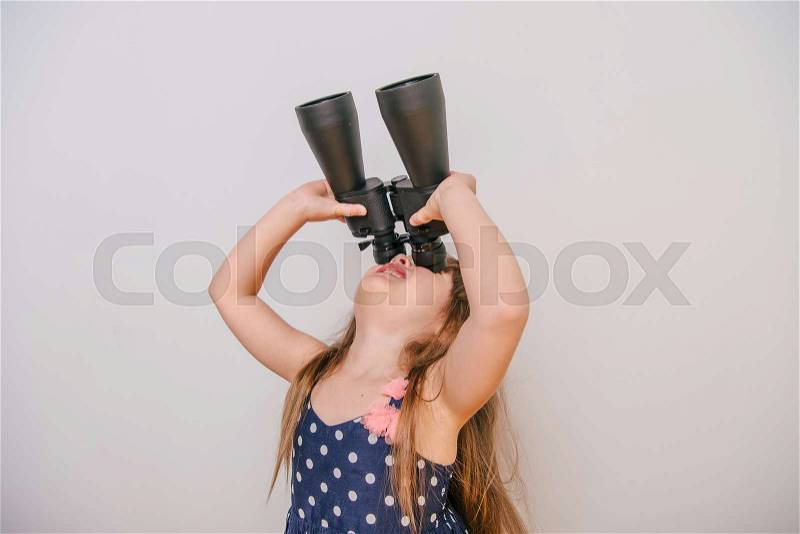 Little girl with binoculars. cute little girl in a dress looks through binoculars. girl watching. a little girl and a large pair of binoculars. polka-dot dress, stock photo