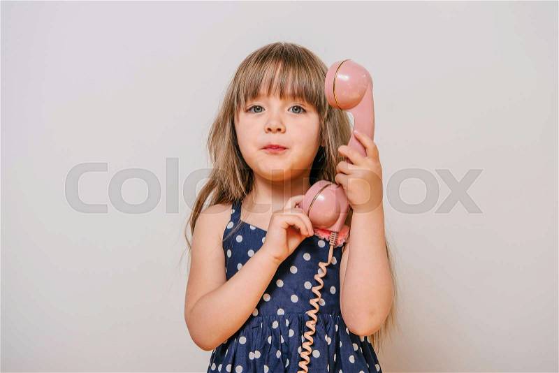 Little girl with the old landline phone. little girl in polka-dot dress. girl talking on retro phone. pink retro phone. girl and pink phone. baby\'s calling on the phone. beautiful girl with long hair, stock photo