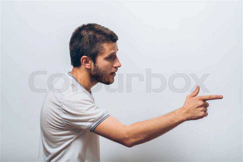 Closeup side view portrait of young man, pointing with finger at someone or something. Positive human face expressions, emotions, feelings, attitude, approach, stock photo