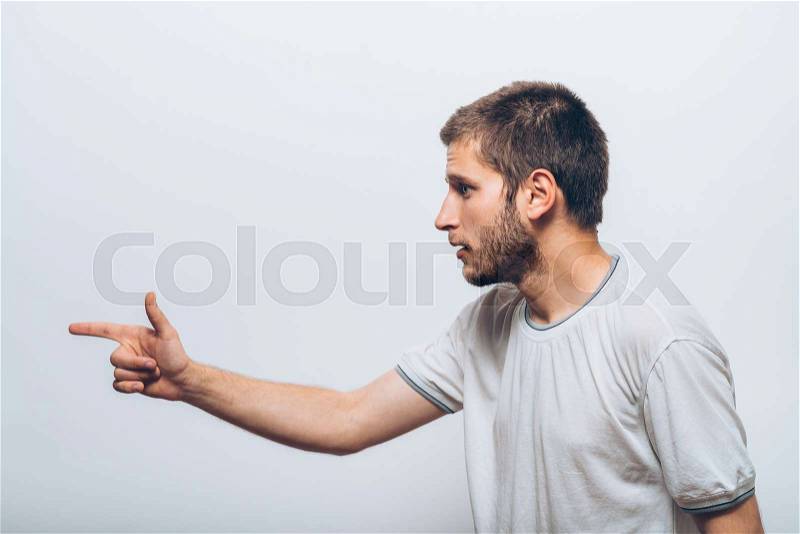 Closeup side view portrait of young man, pointing with finger at someone or something. Positive human face expressions, emotions, feelings, attitude, approach, stock photo