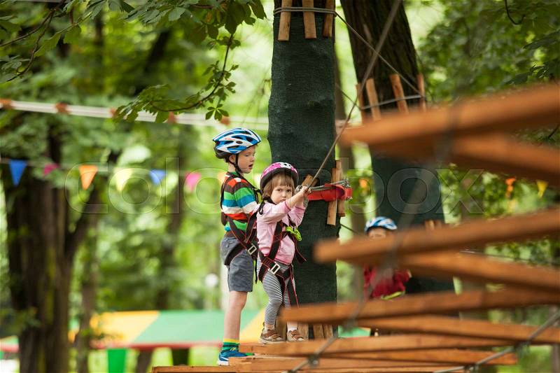 A boy in a helmet and safety equipment in adventure ropes park on the background of nature, stock photo
