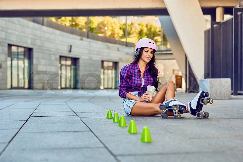 Sport girl resting after rollerblading slalom and drinking coffee. Happy teenager on rollerblading sitting on street a sunny day. Active lifestyle, stock photo