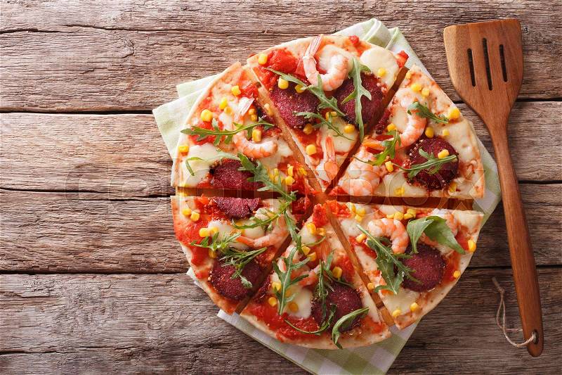 Tasty pizza with salami, shrimp, mozzarella and arugula on a wooden table. horizontal view from above , stock photo