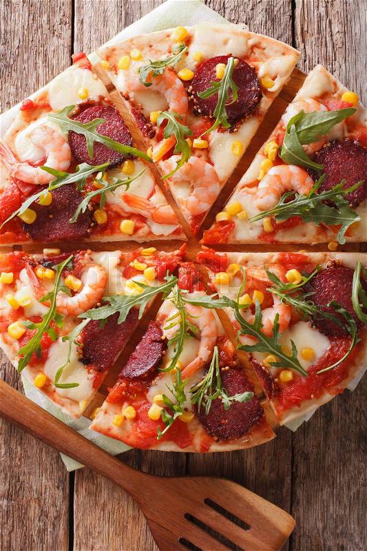 Sliced pizza with shrimp, salami, cheese and arugula close-up on a wooden board. vertical view from above\, stock photo