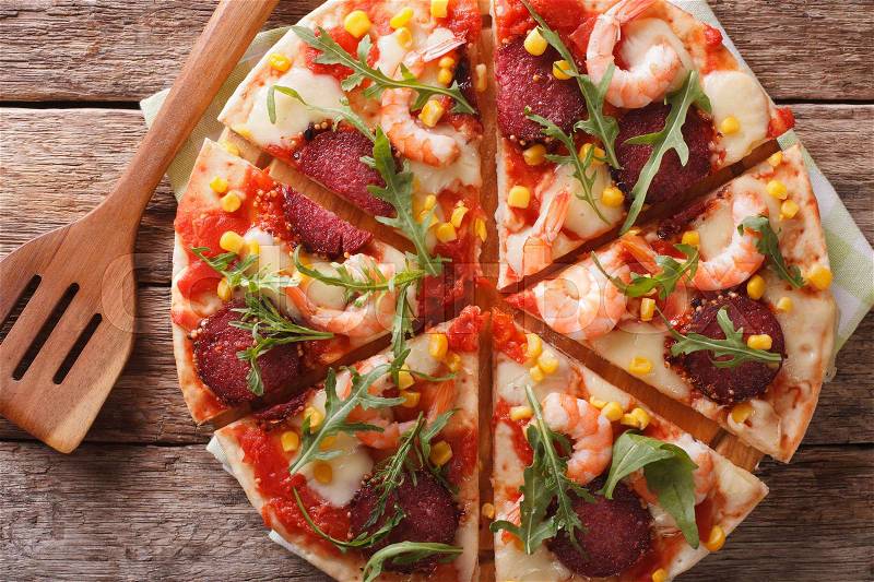 Sliced pizza with shrimp, salami, cheese and arugula close-up on a wooden board. horizontal view from above , stock photo
