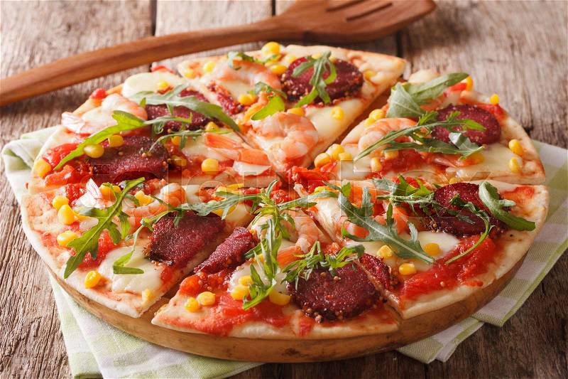Italian pizza with salami, shrimp, corn, mozzarella and arugula close-up on a wooden table. Horizontal , stock photo