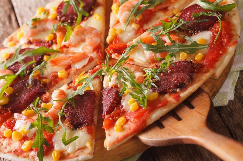 Pizza with shrimp, salami, cheese and arugula macro on a wooden board. horizontal , stock photo