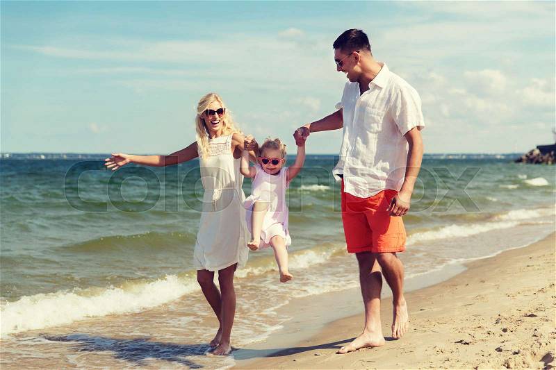 Family, vacation, adoption and people concept - happy man, woman and little girl in sunglasses walking and having fun on summer beach, stock photo