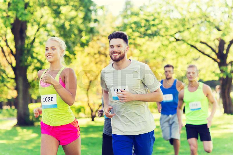 Fitness, sport, friendship, race and healthy lifestyle concept - group of happy teenage friends or sportsmen running marathon with badge numbers outdoors, stock photo