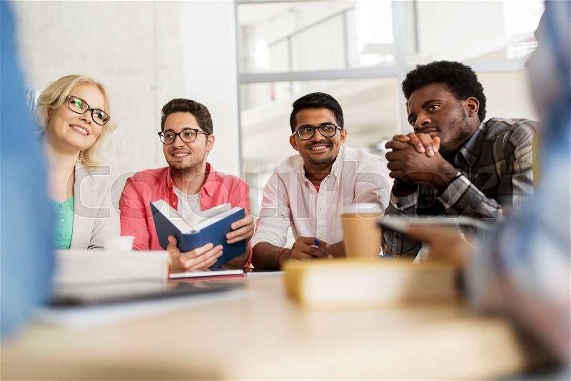 Education, high school, learning, people and technology concept - group of international students sitting at table with coffee and books and talking at university, stock photo