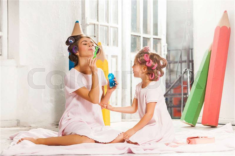 Little smiling girl playing with bubble and her mother on white, stock photo