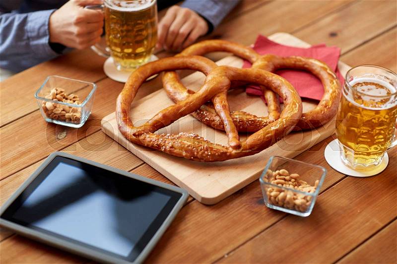 People, leisure, technology and drinks concept - close up of man drinking beer with pretzels, peanuts and tablet pc computer on table at bar or pub, stock photo