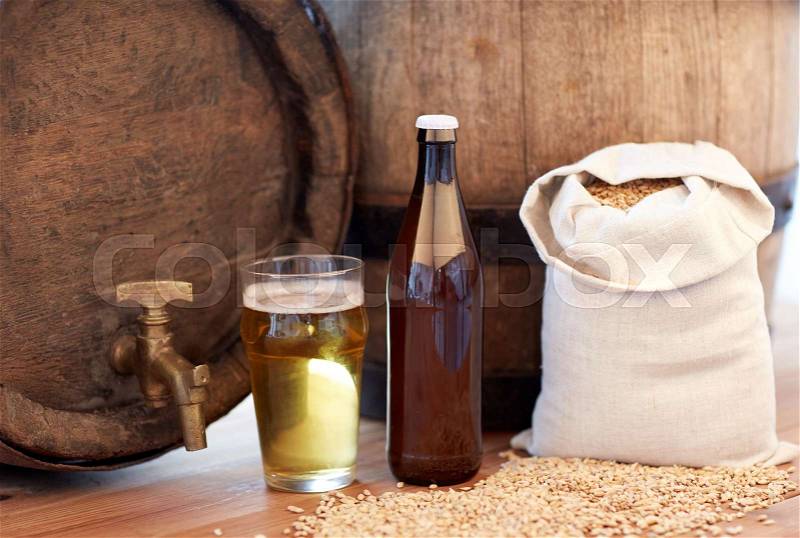 Brewery, drinks and alcohol concept - close up of old beer barrel, glass, bottle and bag with malt on wooden table, stock photo