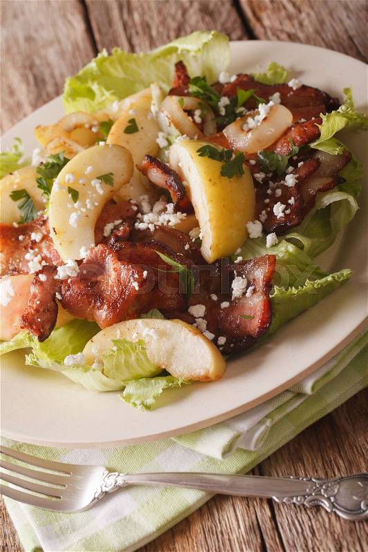 Swedish cuisine salad with fried bacon, onion, green apple and goat cheese close-up on a plate on the table. vertical\, stock photo