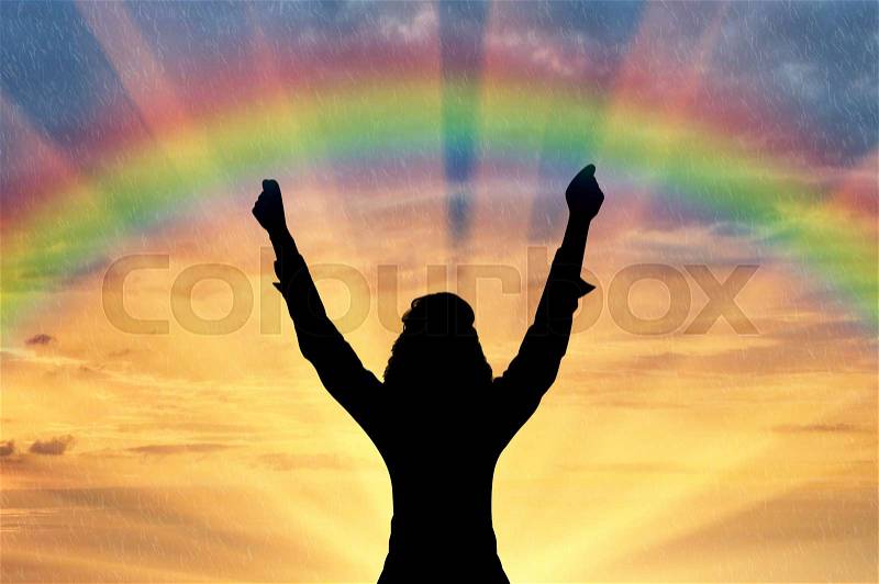 Emotion of happiness. Silhouette of a happy man with his hands up against the sunset and the rainbow, stock photo