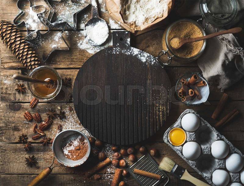 Christmas holiday cooking and baking ingredients. Cookie molds, spices, flour, eggs, cocoa powder, sugar, honey, nuts on old rustic wooden background with dark wood board in center. Top view, copy space , stock photo
