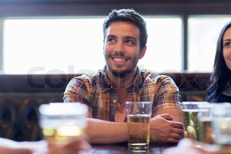 People, leisure, friendship and communication concept - happy man with friends drinking beer and watching sport game or football match at bar or pub, stock photo