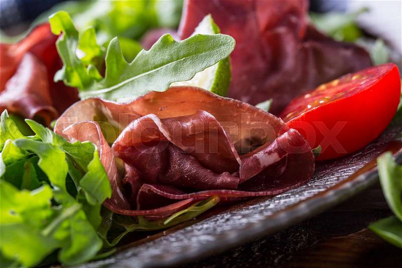 Dried beef bresaola. Salad bresaola arugula baby spinach tomatoes lime and cheese parmesan, stock photo