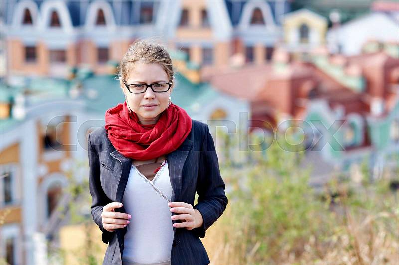 Young woman in glasses and a red scarf on the background of the city, stock photo
