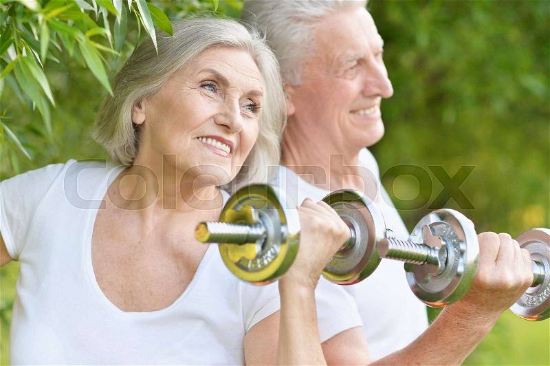 Happy fit senior couple exercising with dumbbells in park, stock photo