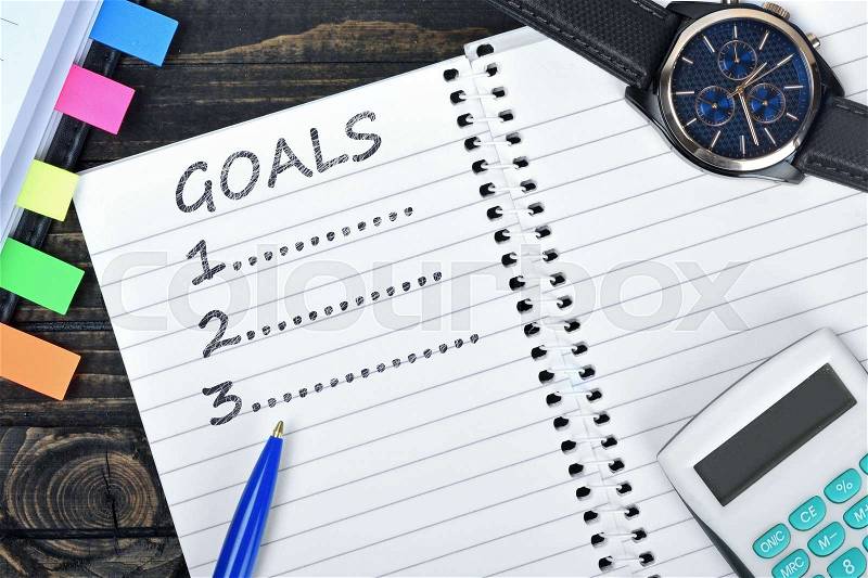 Goals list on notepad and watch on desk, stock photo