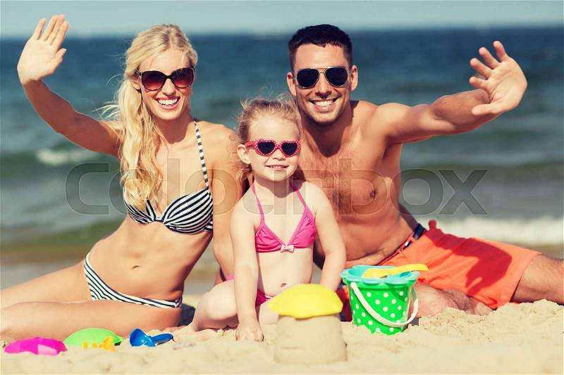 Family, travel, vacation and people concept - happy man, woman and little girl in sunglasses with sand toys waving hands on summer beach, stock photo