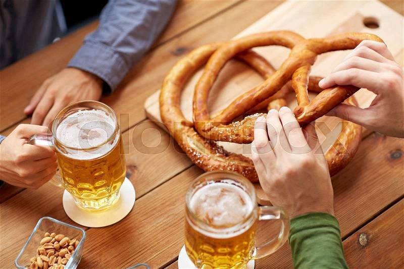 People, leisure and drinks concept - close up of men drinking beer with pretzels at bar or pub, stock photo