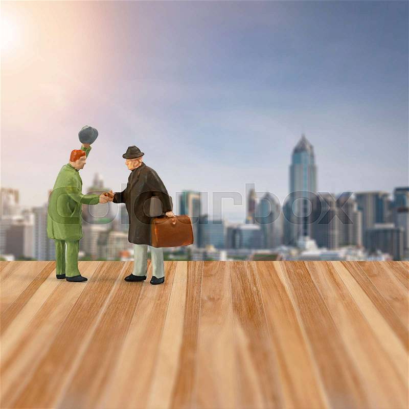 Miniature people figure ,handshake with friend in meeting point ,wooden floor and city background, stock photo