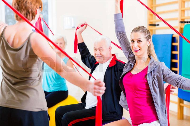 Senior people at fitness course in gym exercising with stretch band, stock photo